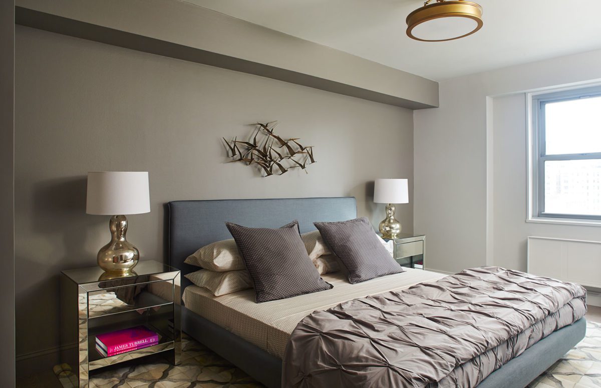 Bedroom with two golden nightstands, a big cozy grey bed, and a window.