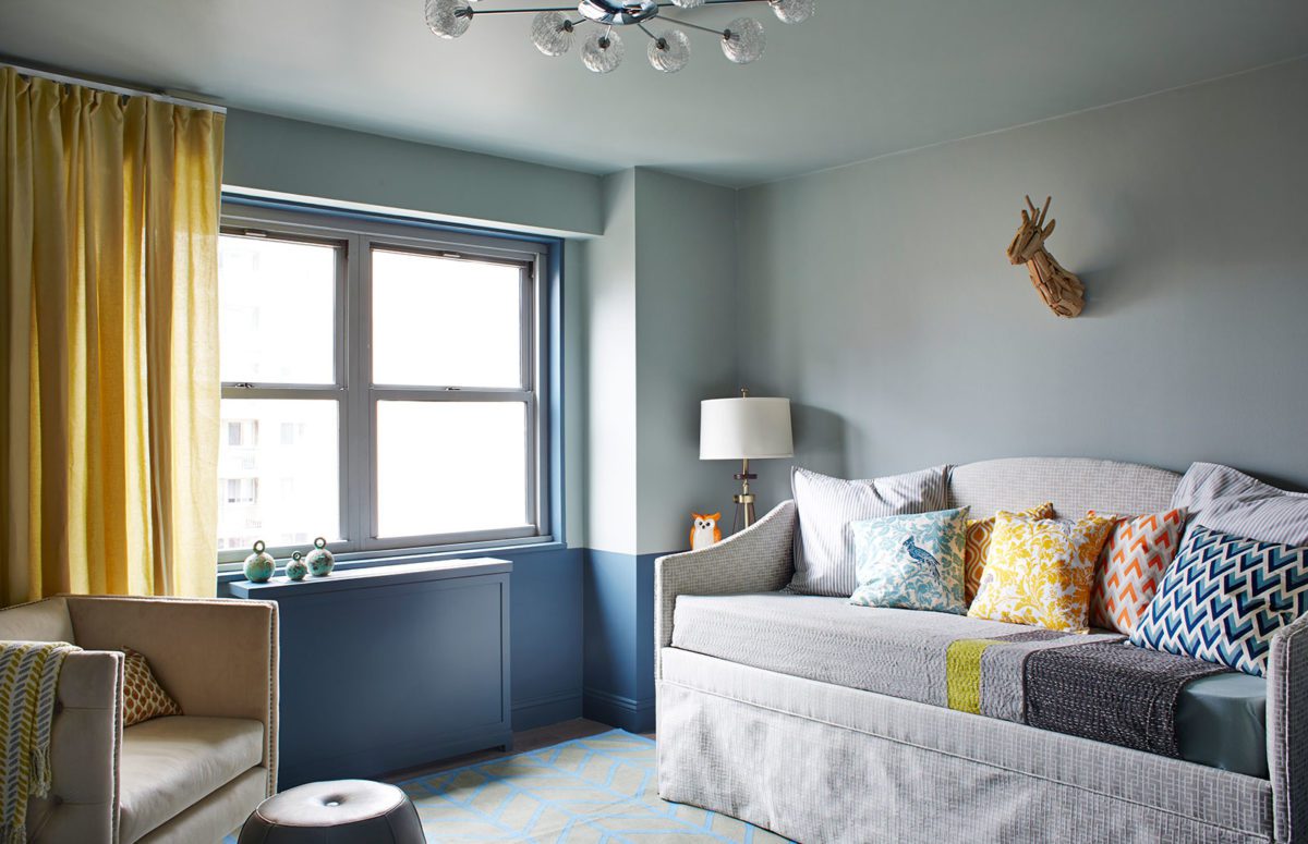 Children's lounge room with a big window, couches, colorful pillows and blue walls.