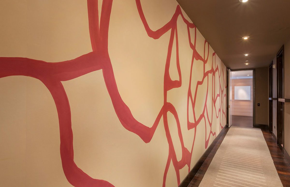 Large Corridor in Warm tones, a beige rug, a big wall with red curvy lines wallpaper and wooden doors
