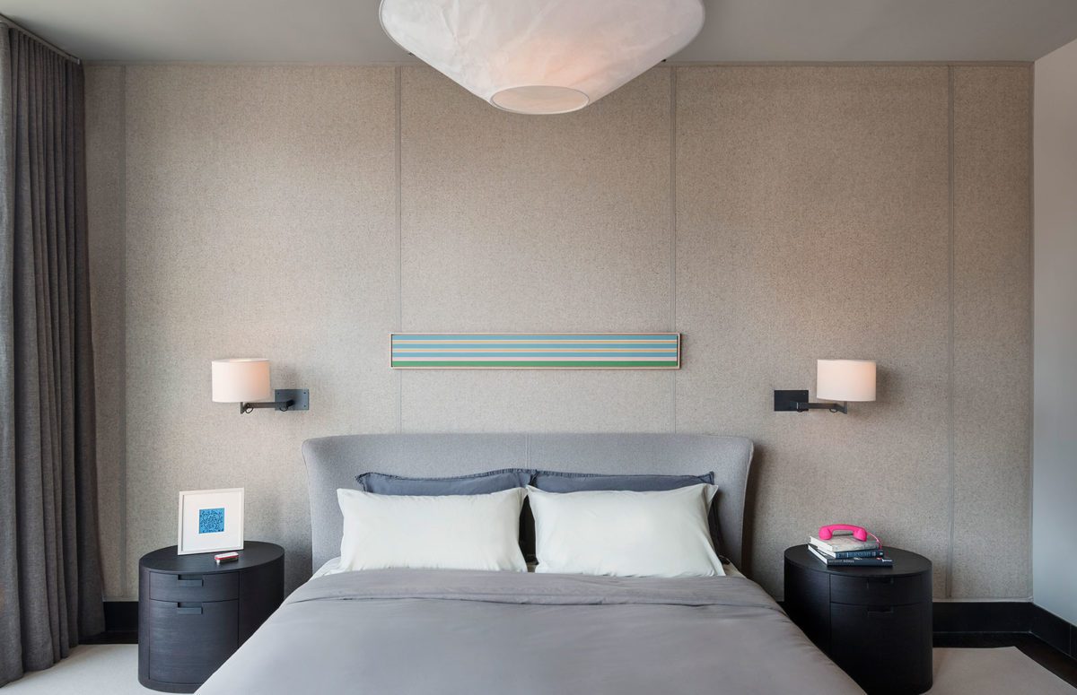 View of a cozy grey bed with light and two black round nightstands on both sides