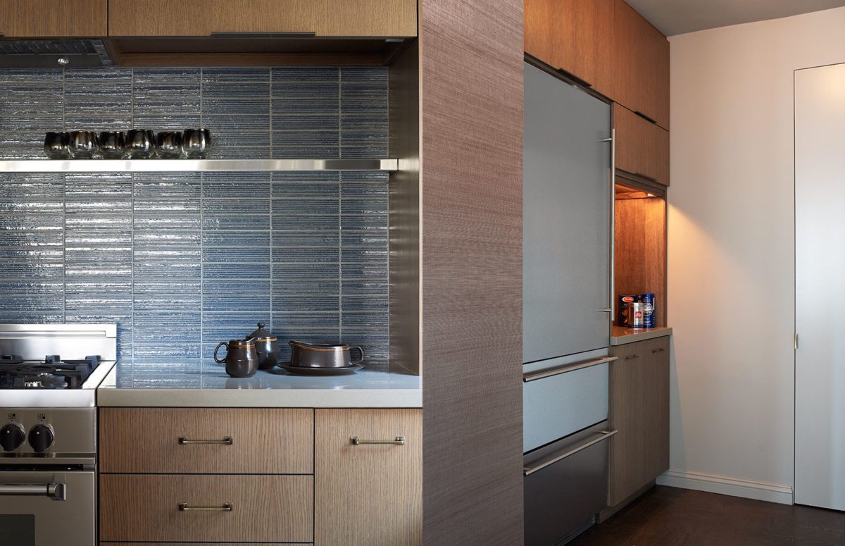 Kitchen counter with wooden cupboard, blue tiles and a big grey integrated fridge