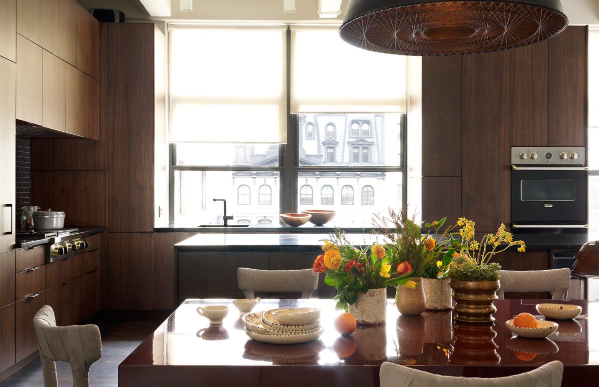 View of Kitchen With Wooden Furniture and Big Dining Table covered with Flowers and Dishes.