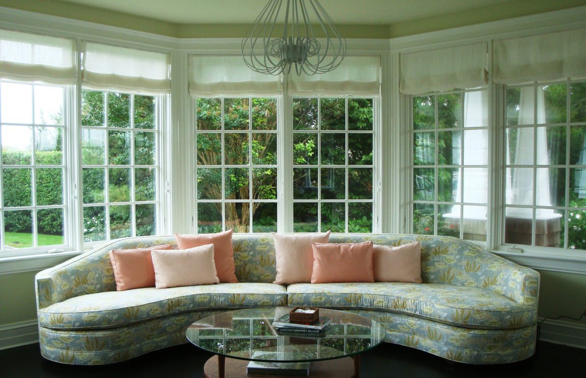 Living Room with Green Interior Design, A Cozy Round Sofa with Six Pink Decorative Pillows, and A Round Crystal Table