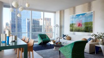 15 Hudson Yards | Livingroom with two green armchairs and a white sofa. Dining table and Brown Chairs to the Left.