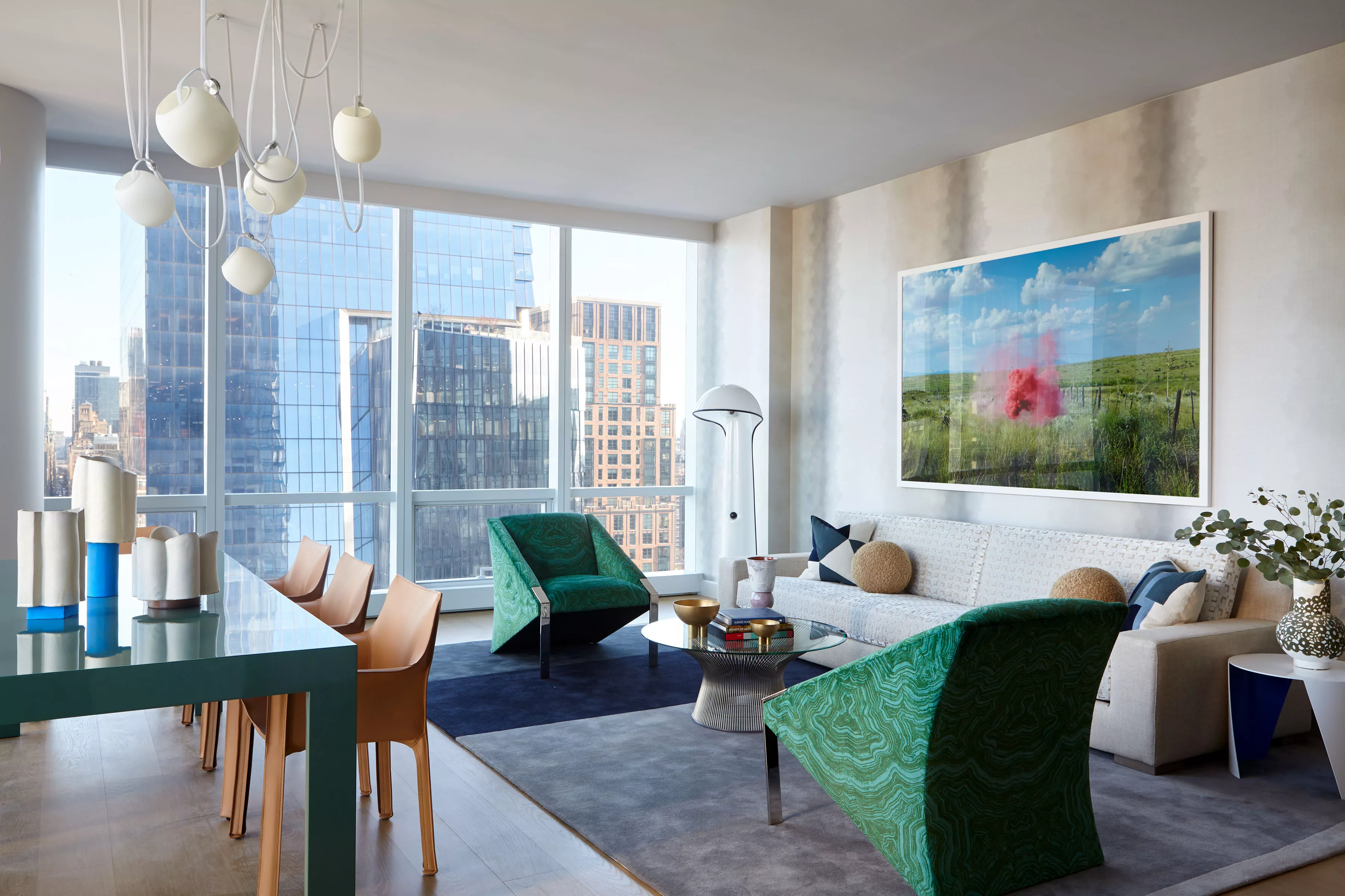 15 Hudson Yards | Livingroom with two green armchairs and a white sofa. Dining table and Brown Chairs to the Left.