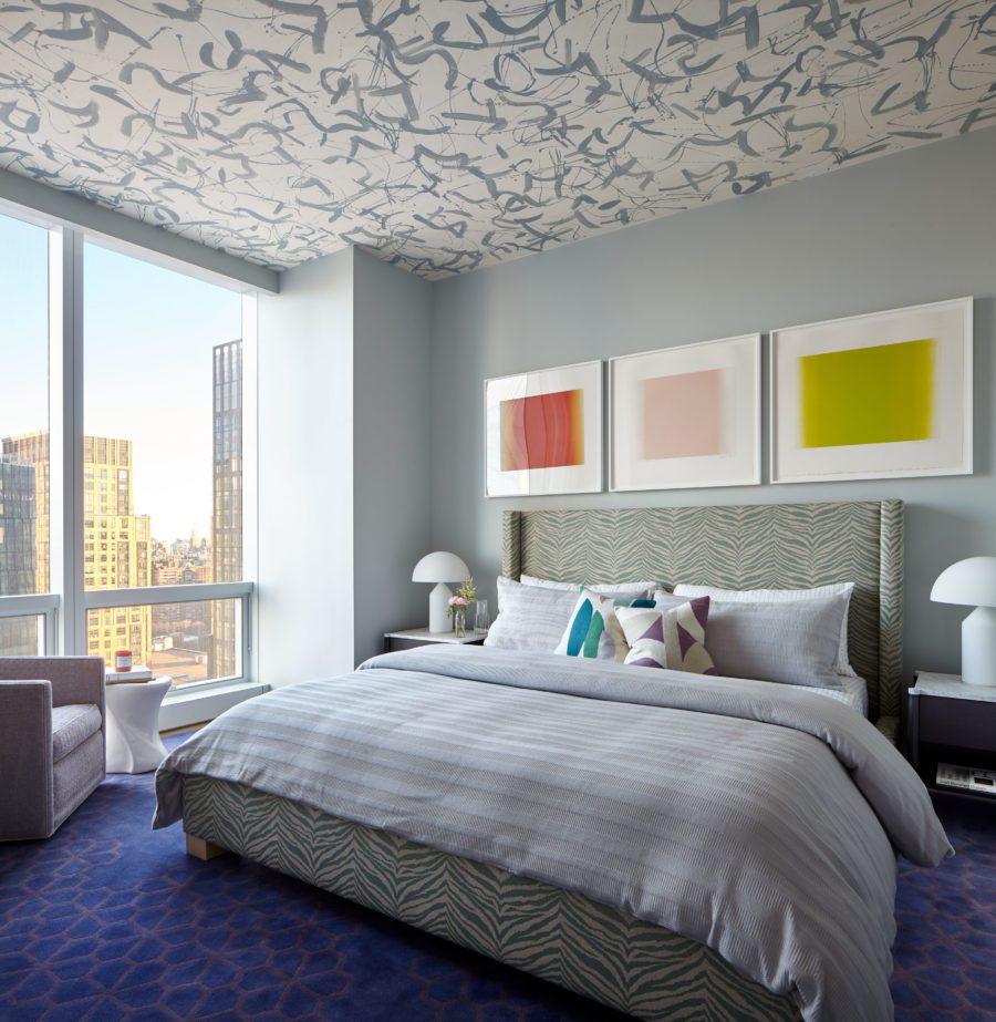 Bedroom setup with A Big Bed in Grey Shades and An Armchair next to the window with a view of the City