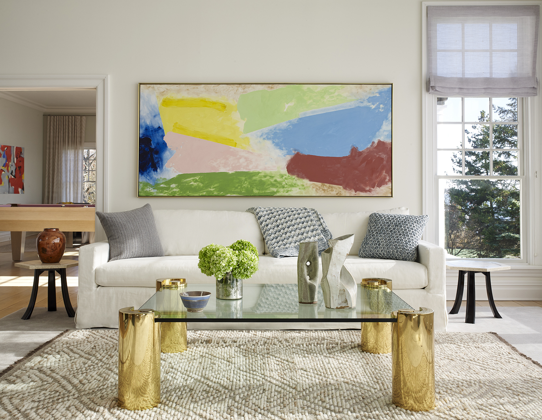 A Living Room with a white sofa, a glass table with golden legs, and a colorful painting.