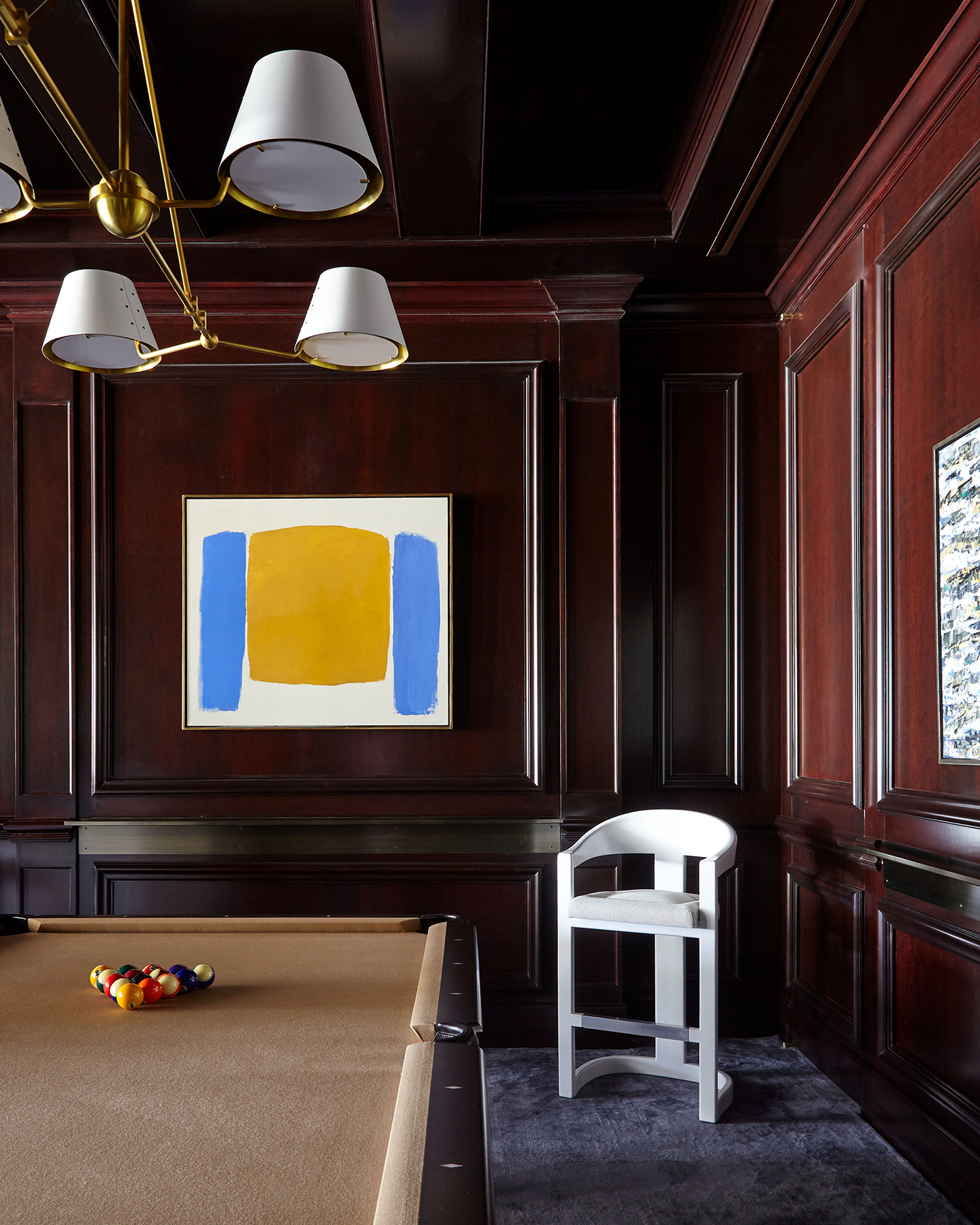 A Dark Billard Room With Wooden Walls, Billard Table, White Chair, and Tricolored Painting.
