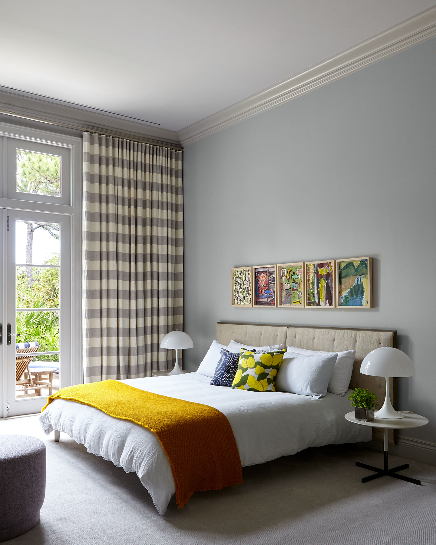 Illuminated Bedroom with Comfortable White Bed, Five Abstract Colorful Paintings, and Striped Curtains in Grey Shades