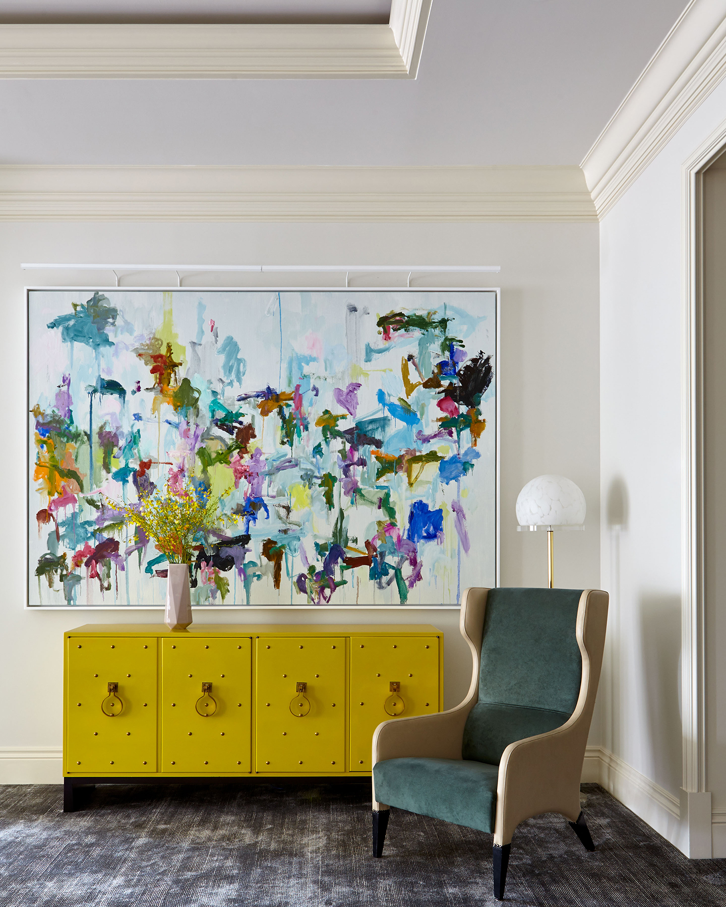 "Bicolored Reading Armchair next to a Mustard-Colored Chest of Drawers and a Huge Vibrant Abstract Painting "