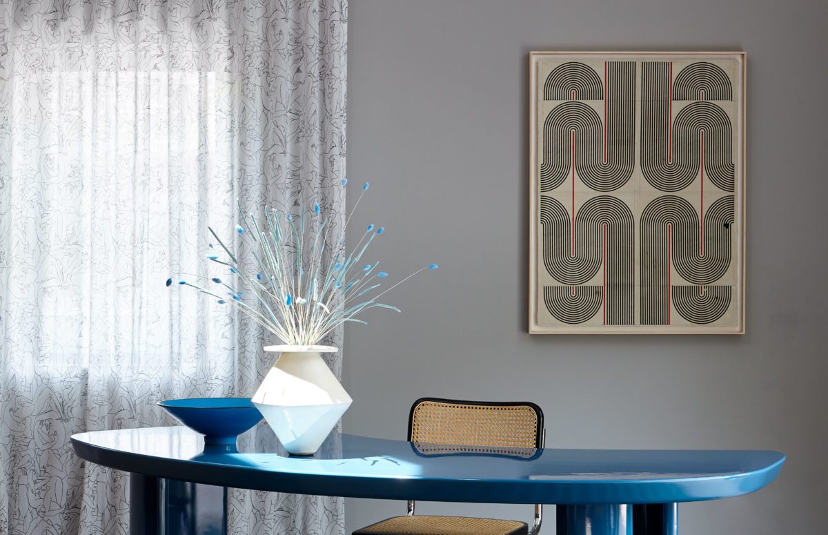 Blue-Colored Flowers in a White Vase on a Blue desk by a gray wall and painting