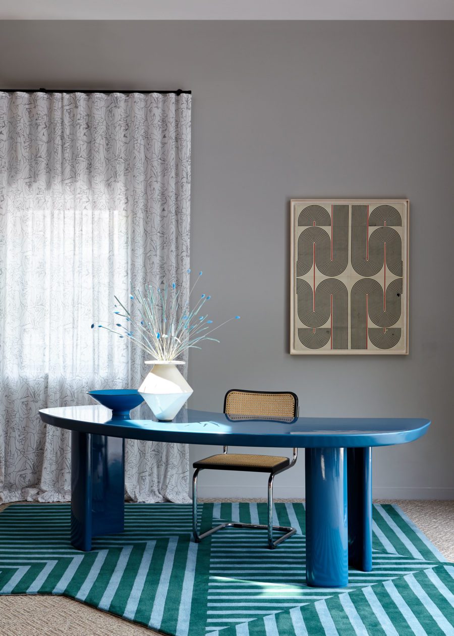 Blue-Colored Flowers in a White Vase on a Blue desk by a gray wall and painting