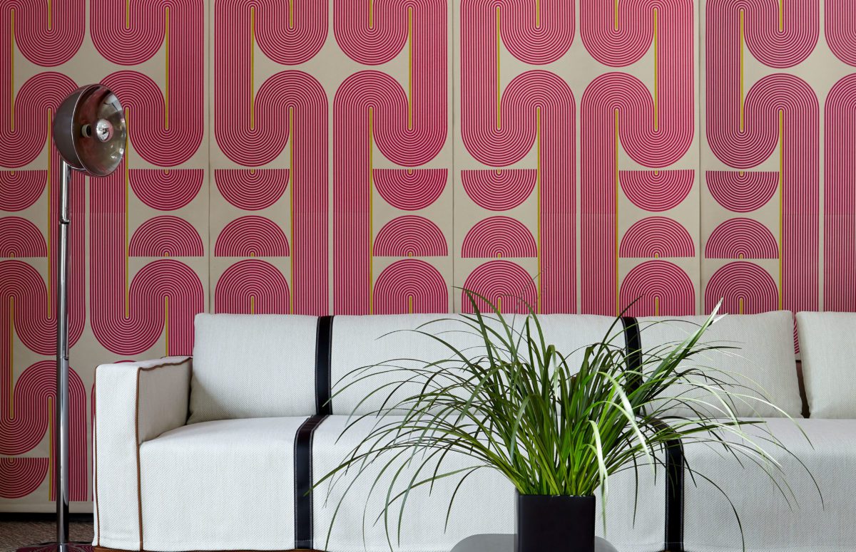 Pink Wallpaper with Repeated Patterns, Big White Sofa, and a Plant in a Black cube-shaped flowerpot on a small grey table.