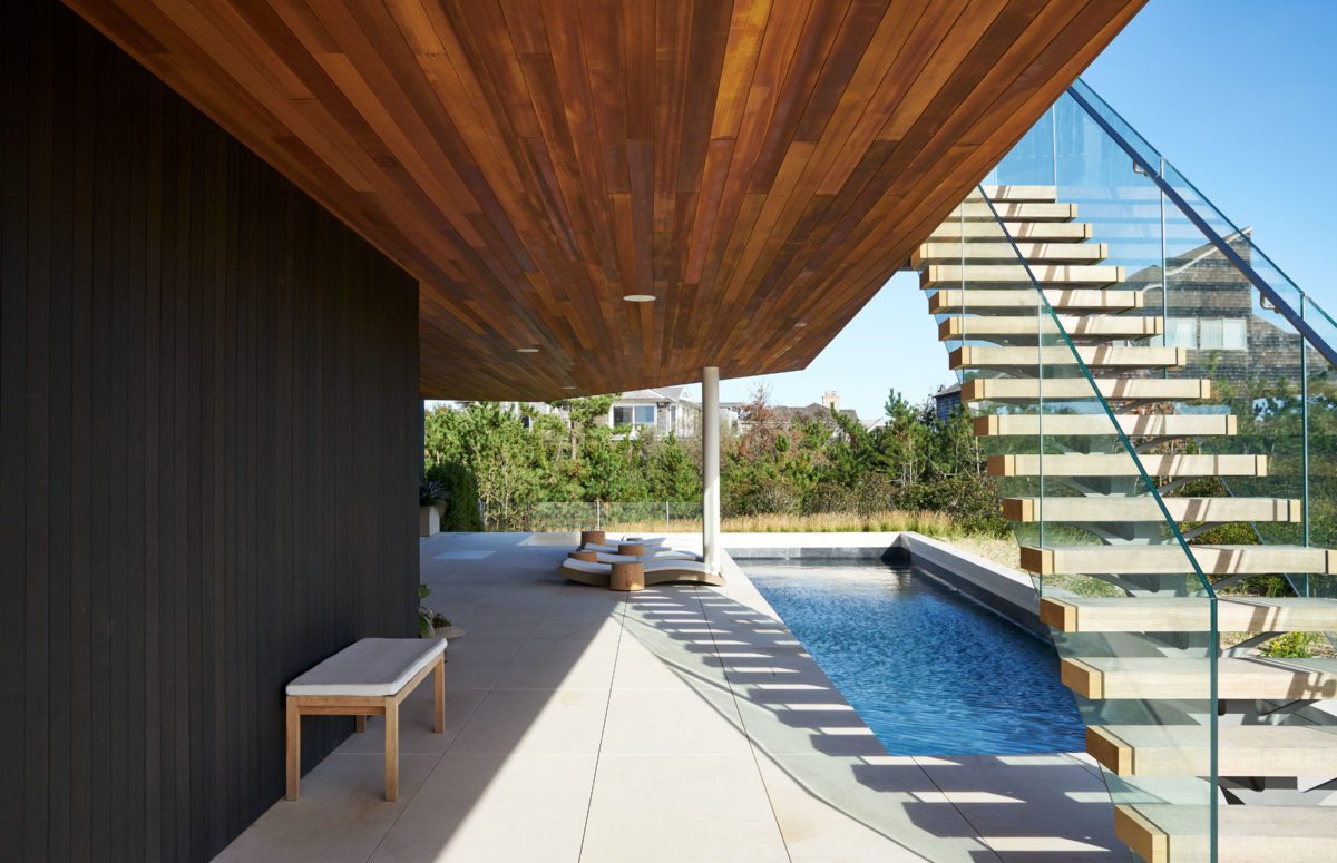 View of deck chairs and a pool beneath stairs outdoors.