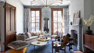 Brooklyn Townhouse | Living Room with White Cozy Sofa and Two Wooden Chairs next to the Fireplace