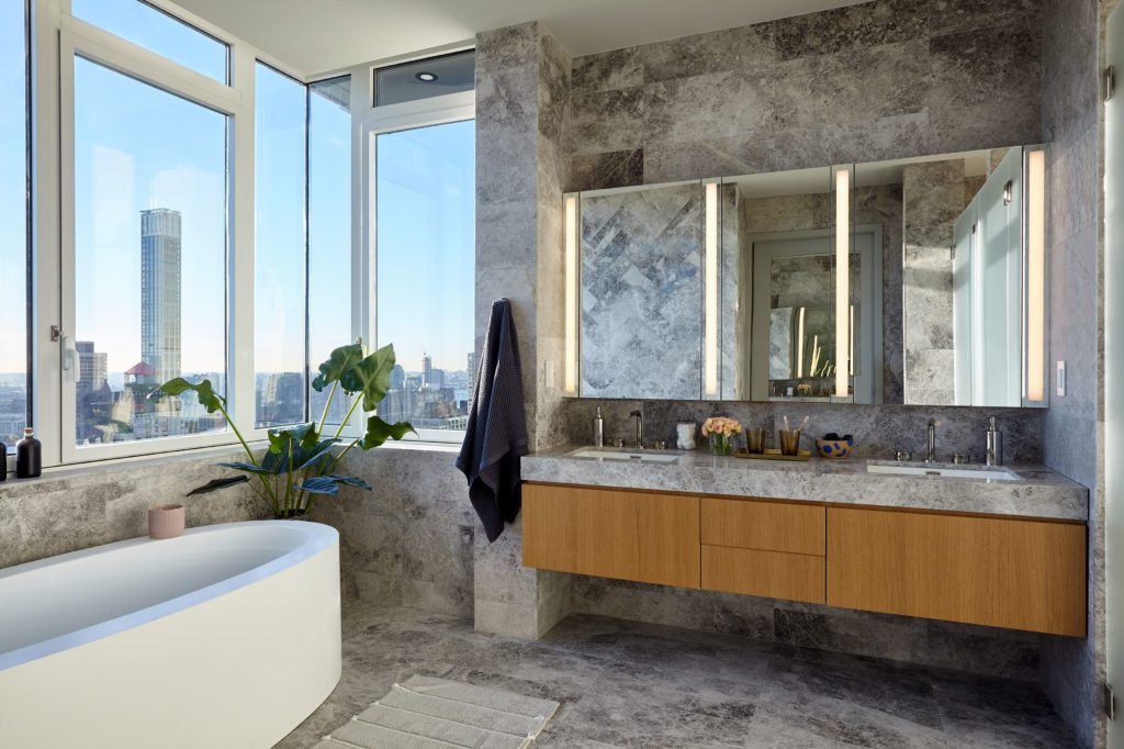 Leyton Bathroom with Grey-texture Tiles and a White Bathtub next to a Window with a view of the City.