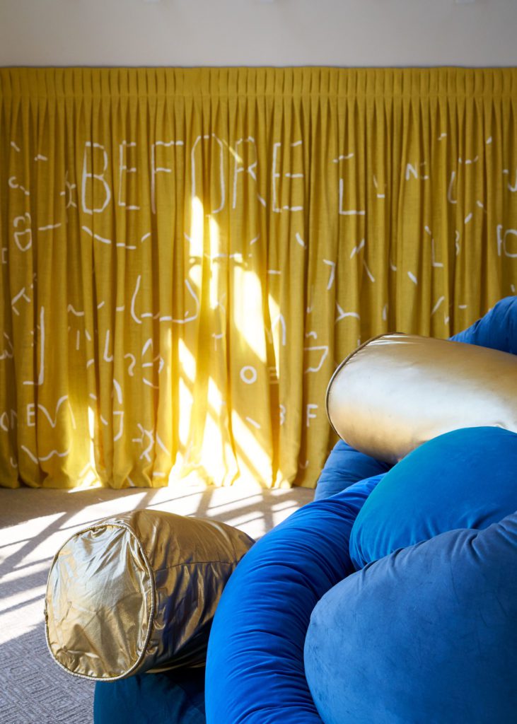 Exhibition The Barn, Zoomed-in View of a Blue and Golden Noodle Pillow, and Yellow Curtains