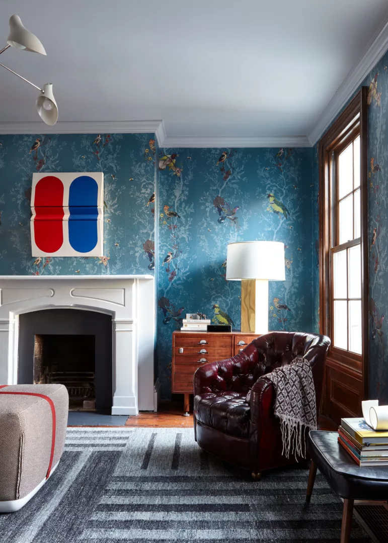 Cozy Brown Leather Reading Armchair, Large White Fireplace, and Blue Ornamental Wallpaper